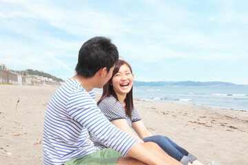 Fototapeta premium Young couple sitting on beach laughing