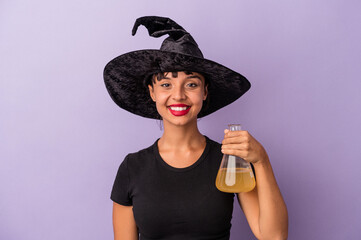 Young mixed race woman disguised as a witch holding potion isolated on purple background  happy, smiling and cheerful.