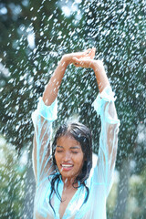 Portrait of young woman in rain with arms raised