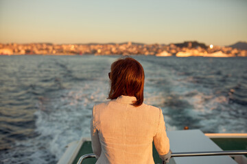 Fototapeta premium Woman with her back on the back of a boat watching as it moves away from the port of the city.