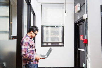 Young man holding laptop in corridor