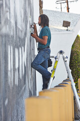 Male african american airbrush artist on step ladders painting mural © Image Source Limited