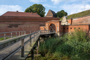 Wooden drawbridge at the entrance gate to the historic brick fortress of Domitz on the river Elbe in Germany, grass and reeds in the moat, blue sky with clouds, copy space,