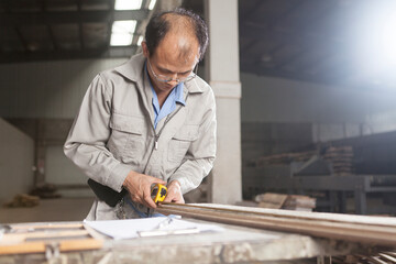 Carpenter measuring wood plank with tape measure in factory, Jiangsu, China