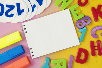 On a painted background among plastic numbers and letters, there is a notebook with a place for text. A marker and a fan of numbers. Educational concept