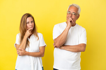 Middle age couple isolated on yellow background having doubts and with confuse face expression