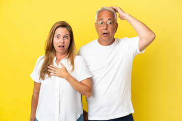Middle age couple isolated on yellow background with surprise facial expression