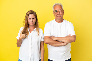 Middle age couple isolated on yellow background annoyed angry in furious gesture