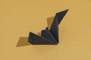 Minimalist Halloween scene with a origami bat made of black paper, isolated on ocher background....