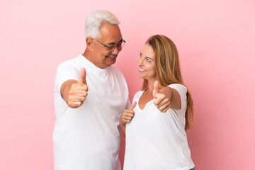 Middle age couple isolated on pink background giving a thumbs up gesture
