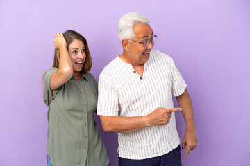 Middle age couple isolated on purple background pointing finger to the side with a surprised face