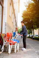 Young man, putting chairs out, outside building