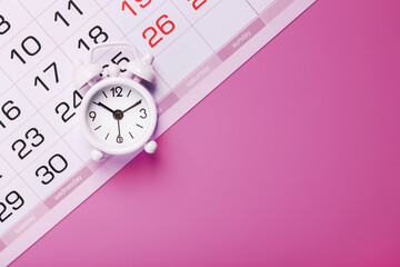 Calendar with a white alarm clock on a pink background.