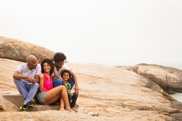 Fototapeta premium Grandfather and family sitting on rock, Ipanema Beach, Rio De Janeiro, Brazil