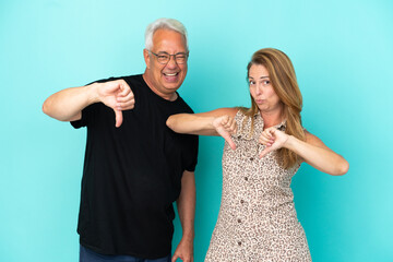 Middle age couple isolated on blue background showing thumb down with both hands