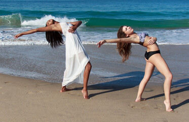Two young female dancers poised bending backwards on beach - obrazy, fototapety, plakaty