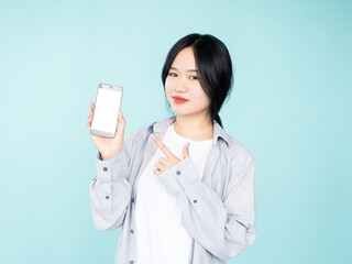 Mobile shopping. Happy asian woman. Online payments. Digital technology. Smiling lady pointing smartphone with blank white screen isolated blue.