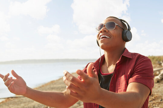Young man on beach wearing headphones and sunglasses, arms raised - a man wearing headphones and lis