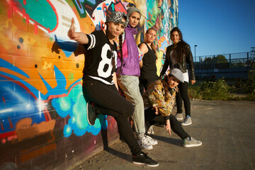 Young women leaning against graffitied wall, looking at camera