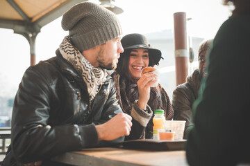 Four young adult friends chatting and eating doughnuts at sidewalk cafe