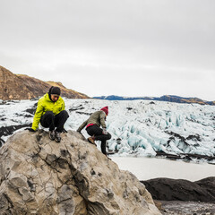 Obraz premium Male and female tourist climbing on boulder at Solheimajokull, Iceland