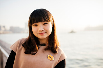 Portrait of young woman with fringe in front of water, looking at camera