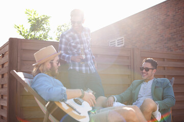 Three male friends chatting and playing guitar at rooftop party
