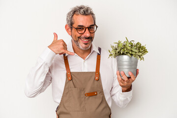Middle age gardener caucasian man holding a plant isolated on white background  showing a mobile...