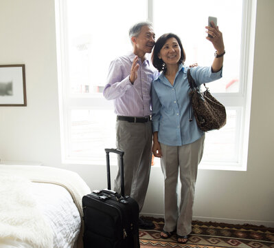Mature couple standing in hotel room using smartphone to take selfie smiling
