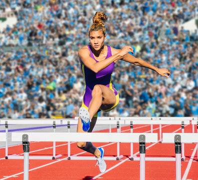 Runner jumping over hurdle on track