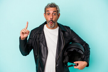 Fototapeta premium Middle age biker caucasian man holding helmet isolated on blue background having some great idea, concept of creativity.