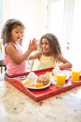 Obraz na płótnie Canvas Sisters at home preparing breakfast, doing high five