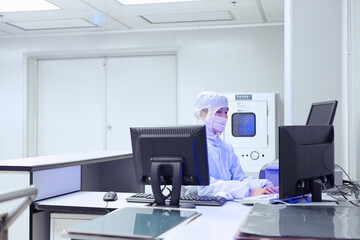 Female factory worker using computer in flexible electronics factory clean room - obrazy, fototapety, plakaty