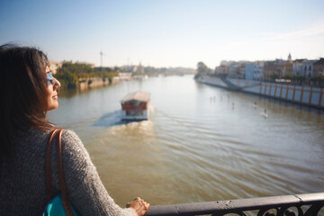 Fototapeta premium Mature female tourist looking out at Guadalqivir river, Seville, Spain