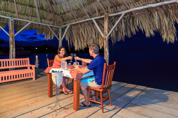Romantic couple raising a champagne toast at waterfront restaurant, St. Georges Caye, Belize, Central America