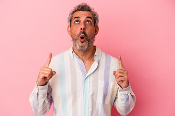 Middle age caucasian man isolated on pink background  pointing upside with opened mouth.