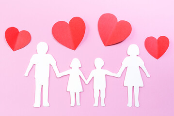 Paper family cut out on bright pink background with paper hearts. Family home, foster care, family mental health, divorce and family crisis concept