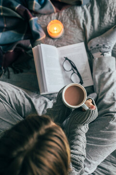 Young girl drinking hot chocolate on cozy bed. Concept of autumn or winter weekend, top view