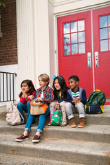 Elementary schoolgirls and boys sitting on elementary school doorway stairs