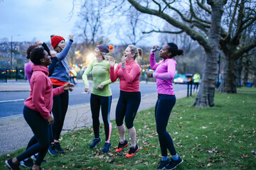Obraz na płótnie Canvas Six female adult runners celebrating on city verge at dusk