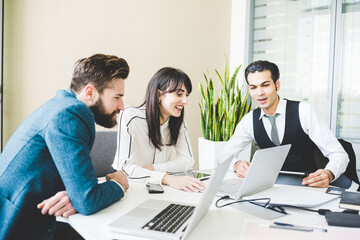 Obraz premium Young businesswoman and men looking at laptop at boardroom table
