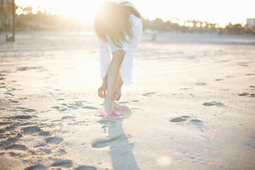 Woman bending to fasten anklet on Santa Monica beach, California, USA - obrazy, fototapety, plakaty