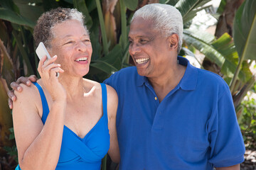 Senior couple sitting outdoors, using smartphone, smiling