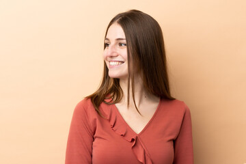 Obraz premium Young caucasian woman isolated on beige background looking to the side and smiling