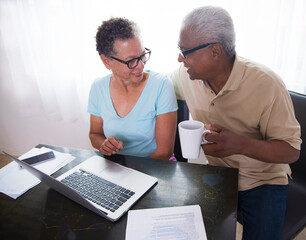 Senior couple sitting at table, using laptop, man holding coffee cup