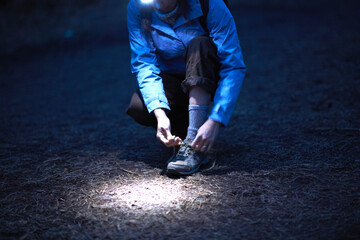 Female hiker wearing head torch tying hiking boot laces at night - obrazy, fototapety, plakaty