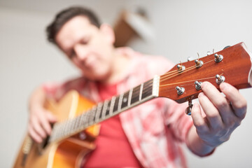 Obraz premium Young man tuning a guitar at home, detail shot with selective focus.