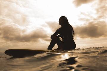 Young woman in sea, sitting on surfboard