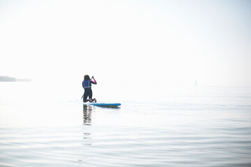 Rear view of female paddleboarder paddling out on misty sea