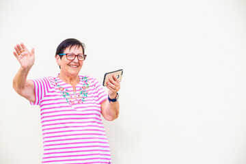mujer mayor sonrie saluda con la mano videollamada con telefono movil aislada en fondo amarillo